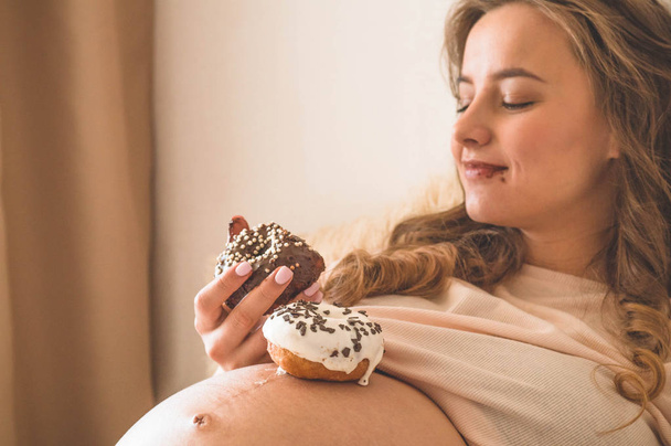 Εγκυμοσύνη και διατροφή. Έγκυος γυναίκα που απολαμβάνει ντόνατς και τσάι στο κρεβάτι, ελεύθερο χώρο. Έννοια της προσδοκίας και της υγείας - Φωτογραφία, εικόνα