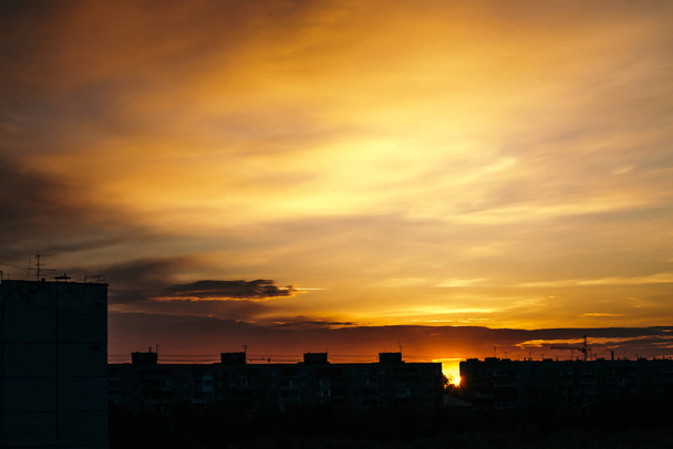 Όμορφο συννεφιασμένο δραματικό πρωινό ουρανό πάνω από τη σιλουέτα των κτιρίων της πόλης. Γραφική αυγή στην πόλη. Ίχνη αεροσκαφών σε ζωηρά σύννεφα. Φόντο από αδιανόητη Ανατολή του ήλιου στον ουρανό. - Φωτογραφία, εικόνα