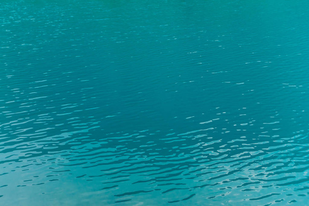 Lesklá textura azurového povrchu horského jezera. Minimalistický základ s odrazem hor v čisté vodě za slunečného dne. Kopírovat místo. - Fotografie, Obrázek