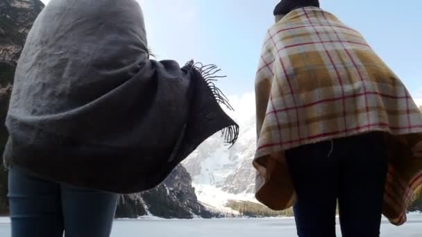 zwei reisende junge Freundinnen in Decken gehüllt zum zugefrorenen See - Filmmaterial, Video