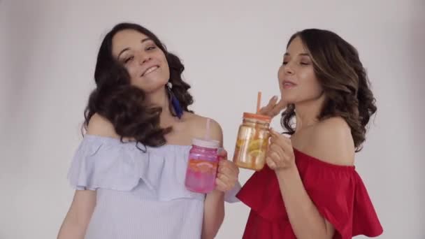 Dwie młode siostry piją świeży sok pomarańczowy - Materiał filmowy, wideo