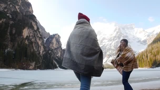 Dos jóvenes viajeras cubiertas de mantas que caminan por la costa del lago congelado
 - Metraje, vídeo