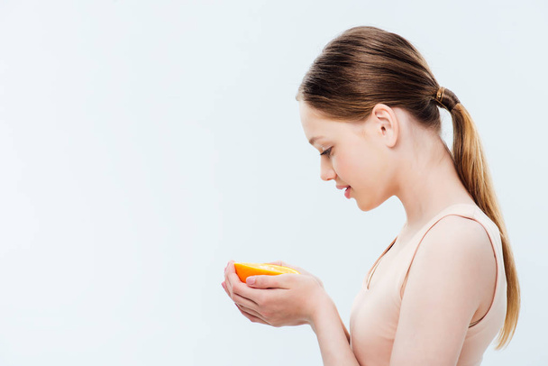 side view of teenager holding orange half isolated on grey - Foto, imagen