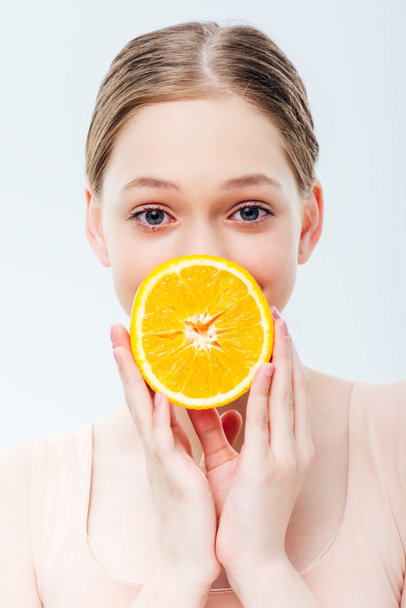 dospívající dívka držící zralou oranžovou před ústy izolovaná na šedé - Fotografie, Obrázek