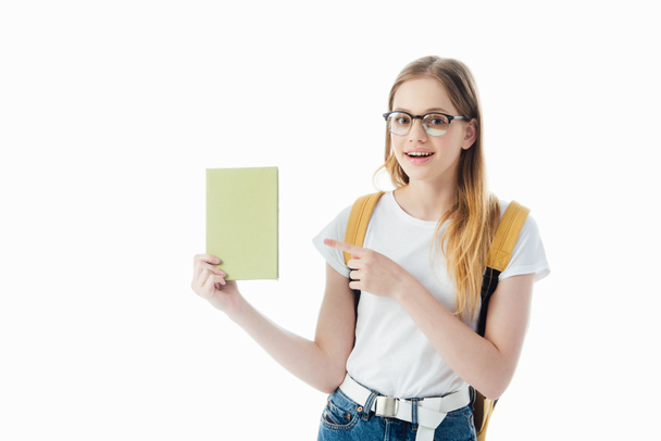 smiling schoolgirl with backpack pointing with finger at book isolated on white - Fotografie, Obrázek