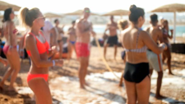 Defocused image of big group of people dancing on the sea beach disco party. People having fun during summer holiday vacation - Photo, Image