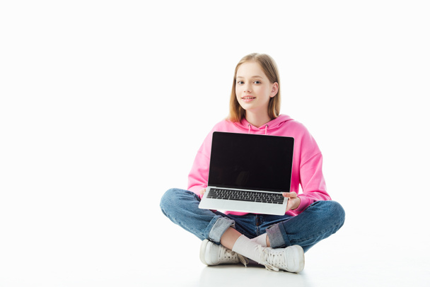 smiling teenage girl with crossed legs holding laptop with blank screen isolated on white, illustrative editorial - Фото, изображение