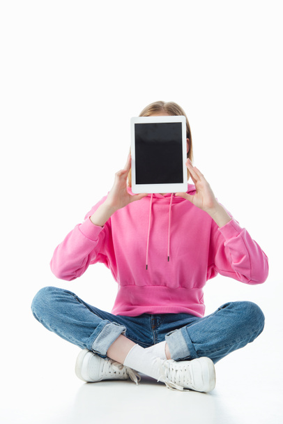 Teenager-Mädchen in Lotus-Pose hält digitale Tablette mit leerem Bildschirm isoliert auf weiß - Foto, Bild