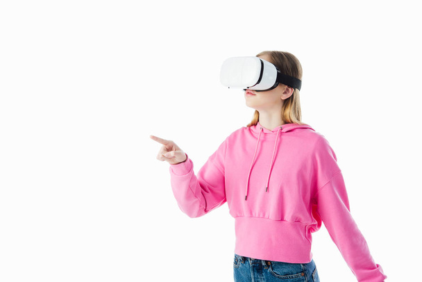 teenage girl in pink hoodie wearing vr headset and pointing with finger isolated on white - Foto, Bild