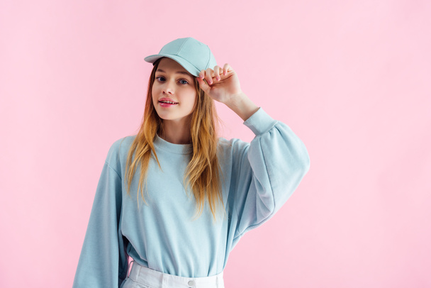 smiling pretty teenage girl touching cap isolated on pink - Foto, Bild