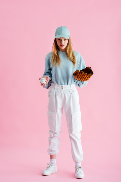 pretty teenage girl in cap holding baseball glove and ball on pink - Foto, Imagen