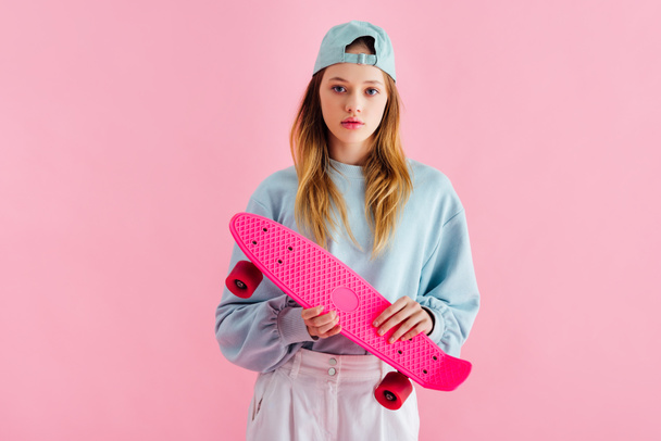 pretty teenage girl in cap holding penny board isolated on pink - Foto, Bild