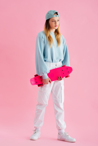 pretty teenage girl in cap holding penny board on pink - Photo, Image
