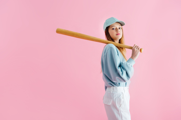 pretty teenage girl in cap holding wooden baseball bat isolated on pink - Photo, Image