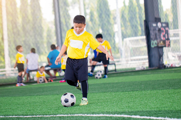 アジアの子供のサッカー選手のスピードランでぼやけたボールは、ボールを撃つために実行します - 写真・画像