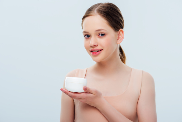 cheerful teenage girl holding cosmetic cream isolated on grey - Fotografie, Obrázek