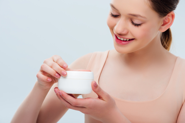 happy teenage girl holding cosmetic cream isolated on grey - Photo, Image