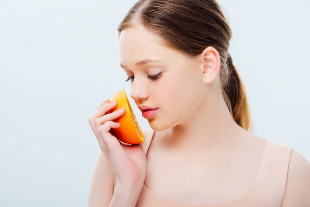 beautiful teenage girl looking at ripe orange half isolated on grey - Photo, Image