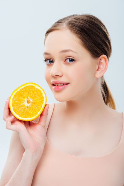 smiling beautiful teenage girl holding ripe orange half isolated on grey - Foto, immagini