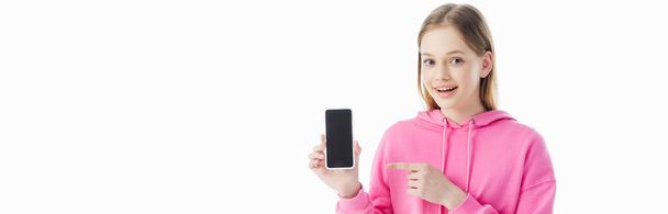 panoramic shot of happy teenage girl in pink hoodie pointing with finger at smartphone isolated on white - 写真・画像