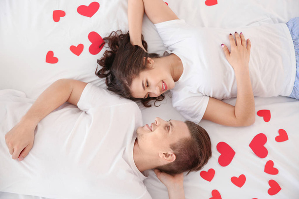 Happy young couple with paper hearts lying in bed - Fotografie, Obrázek