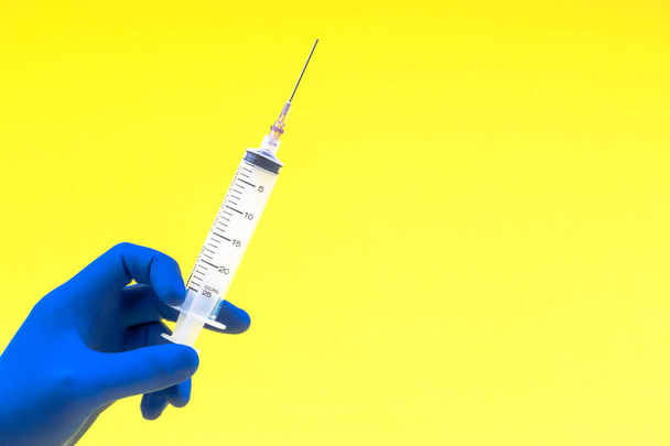 Hand in a blue glove holding syringe on yellow background - Photo, Image