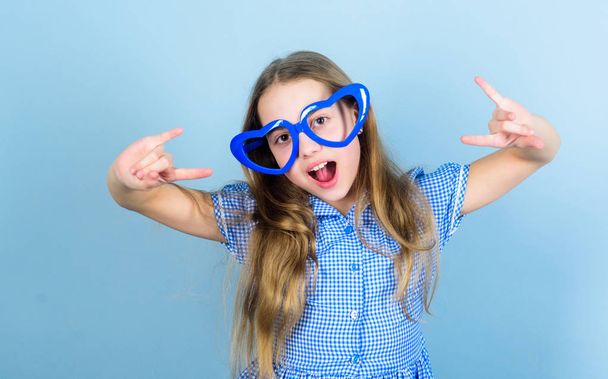 Power of love. Kid girl heart shaped eyeglasses. Girl adorable smiling face fall in love. Child charming smile blue background. Kid happy lovely enjoy childhood. Heart symbol of love. Fashion eyewear - Фото, изображение