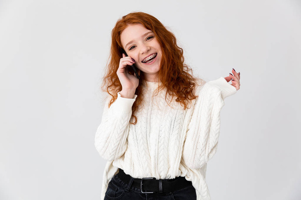 Girl redhead posing isolated over white wall background talking by phone. - Foto, Bild