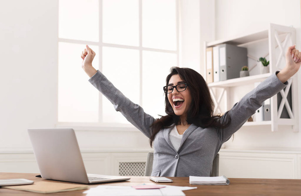 Imprenditrice eccitata che celebra il successo con mani alzate sul posto di lavoro
 - Foto, immagini