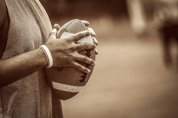 American Football-Spieler hält den Ball zwischen seinen Händen auf einem Duoton-braunen Farbstil - Foto, Bild