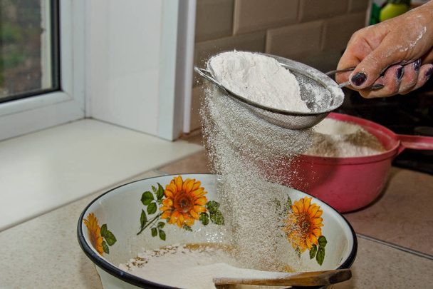 female hand sifting flour through manual flour sieve in a bowl close-up copy space. cooking dough. metal kitchen appliance - Zdjęcie, obraz