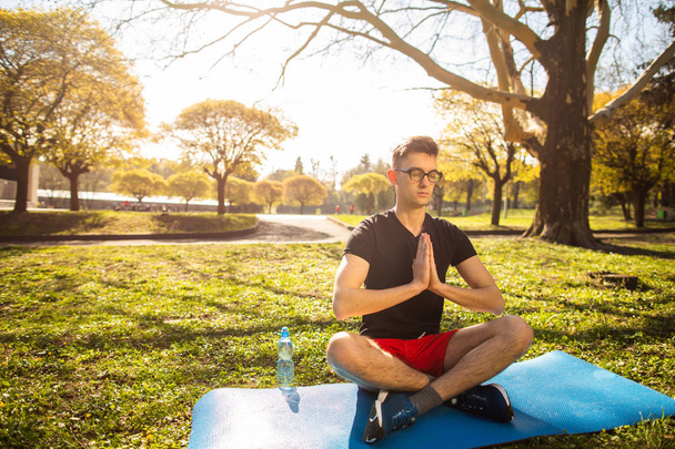 A young man relaxes and doing yoga in the green park. Concept of a healthy lifestyle - 写真・画像