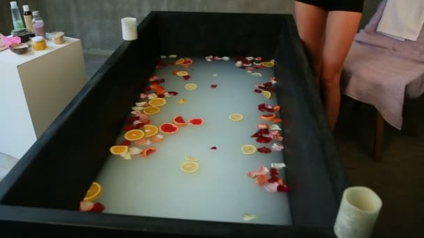 hubená holka hází citrusové plátky a plátky růží v černé lázni - Záběry, video
