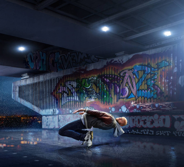Bailarina de Hip Hop masculina. Hermoso hombre bailando de noche sobre el fondo de la pared de graffiti
 - Foto, imagen