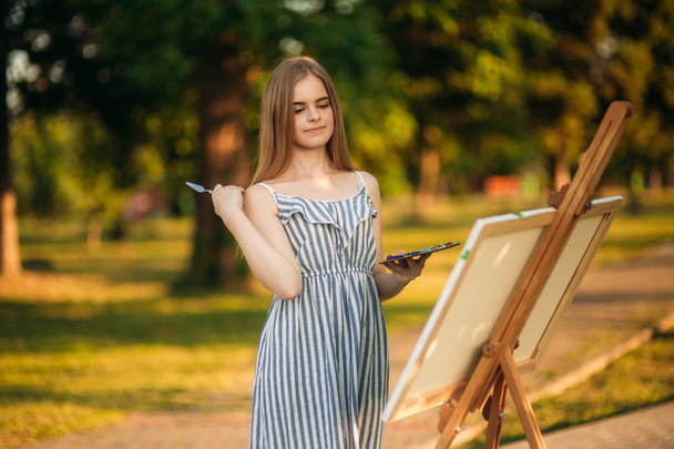 Blond haar meisje in jurk tekening van een afbeelding in het park - Foto, afbeelding