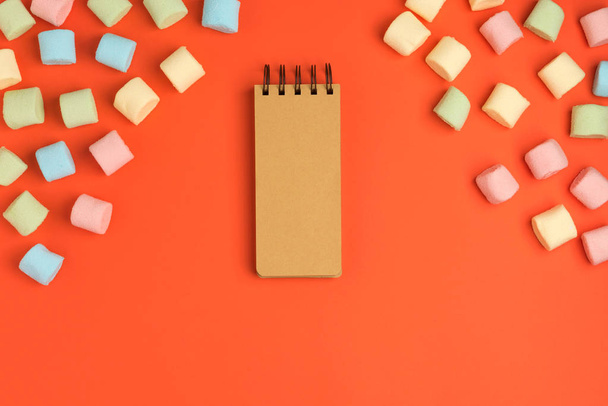 Coral paper background with marshmallow and notepad. Place for your text. Cozy sweet background - 写真・画像