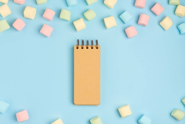 Blue paper background with marshmallow and notepad. Place for your text. Cozy sweet background - 写真・画像