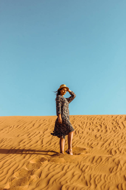 Young beautiful girl in a long dress and a hat in the middle of the desert during the daytime - Фото, зображення