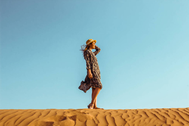 Young beautiful girl in a long dress and a hat in the middle of the desert during the daytime - Fotografie, Obrázek