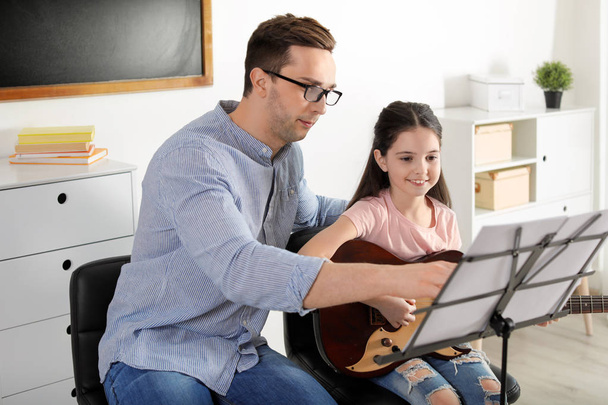 Little girl playing guitar with her teacher at music lesson. Learning notes - Foto, imagen