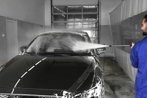 Worker cleaning automobile with high pressure water jet at car wash - Photo, image