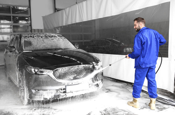 Worker cleaning automobile with high pressure water jet at car wash - Fotó, kép