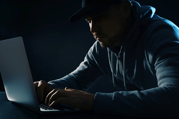 Man using laptop at table on dark background. Criminal activity - Photo, Image