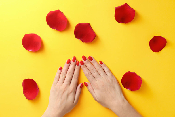 Woman holding hands near rose petals on color background, top view. Beautiful nail polish - Foto, immagini