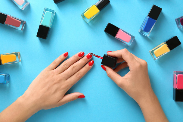 Woman applying bright nail polish on color background, top view - Φωτογραφία, εικόνα