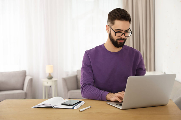 Handsome young man working with laptop at table in home office - Φωτογραφία, εικόνα