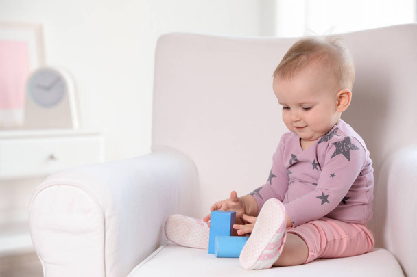 Cute baby girl playing with building blocks in armchair at home. Space for text - Photo, image