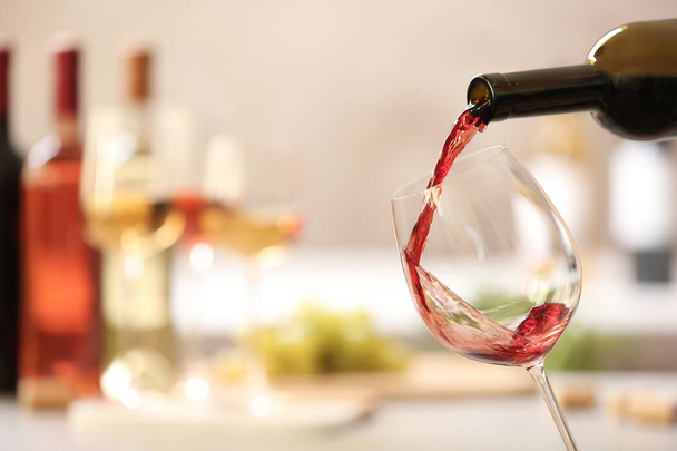 Pouring red wine from bottle into glass on blurred background. Space for text - Фото, зображення