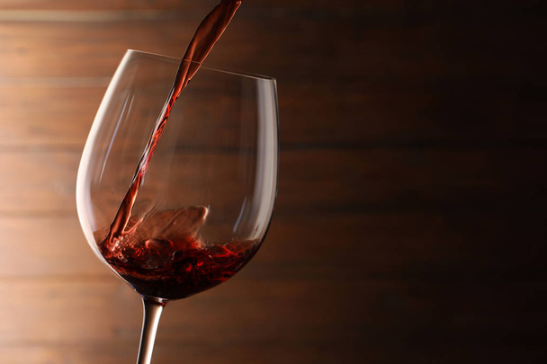 Pouring red wine into glass on blurred background. Space for text - Foto, afbeelding