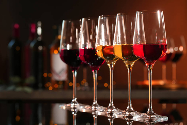Rivi lasit eri viinejä baaritiskillä vastaan hämärtynyt tausta. Tekstitila
 - Valokuva, kuva